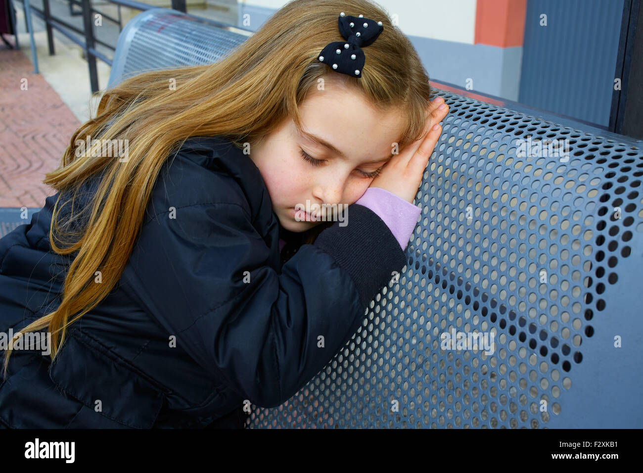 Kid girl blonde prétendant être dormir sur un banc de la rue Banque D'Images