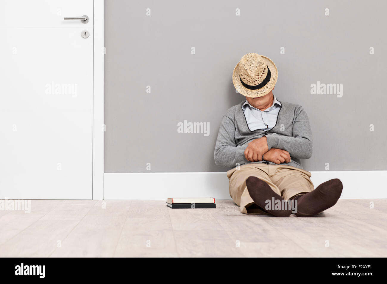 Hauts de dormir sur le plancher avec son chapeau couvrant son visage et appuyé contre un mur à côté d'une porte blanche Banque D'Images