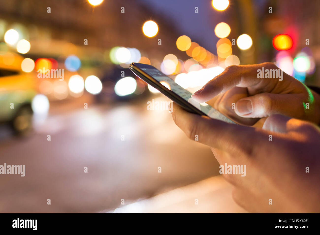 L'homme en utilisant son téléphone portable dans la rue, nuit lumière arrière-plan flou Banque D'Images