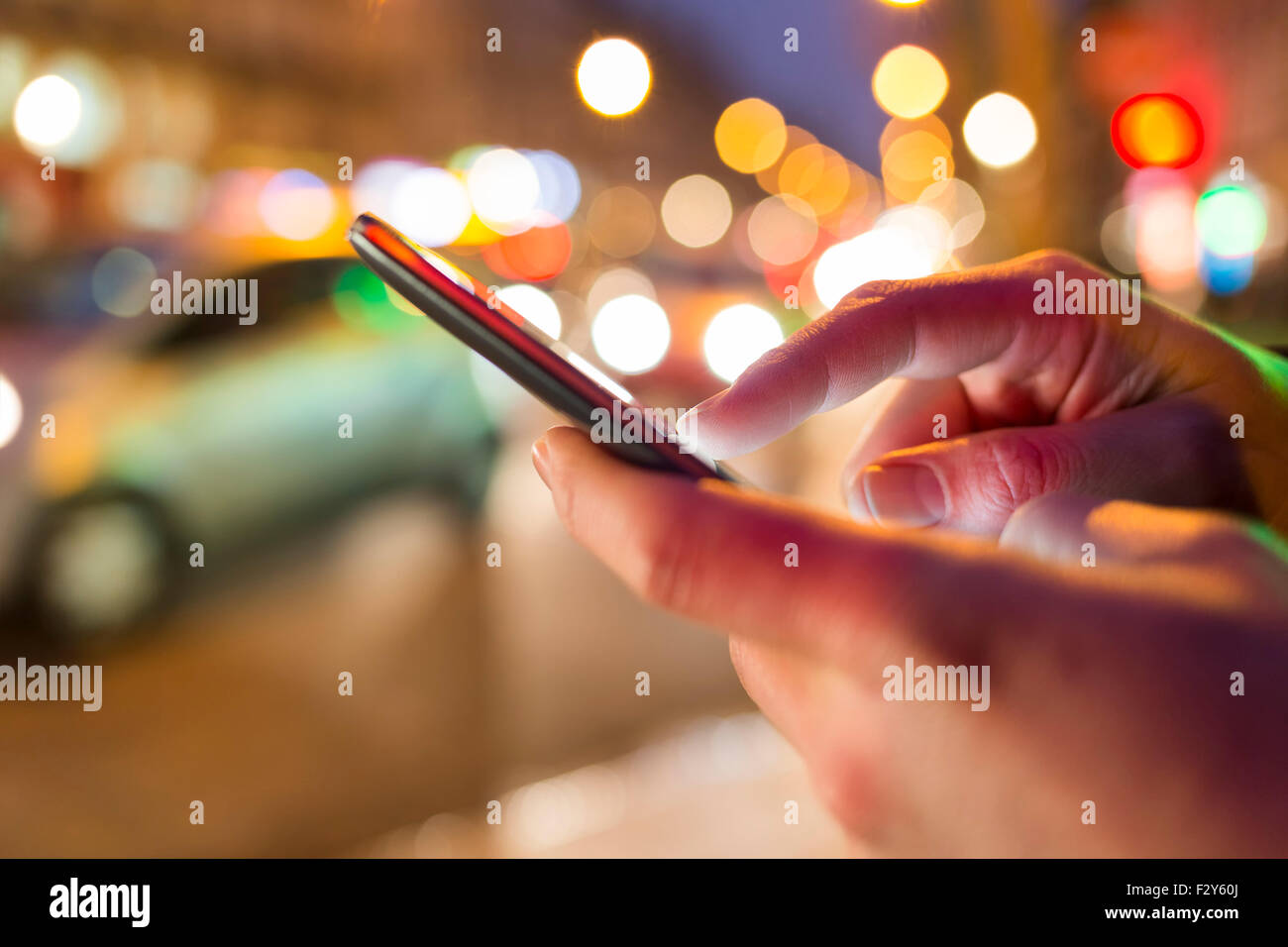 L'homme en utilisant son téléphone portable dans la rue, nuit lumière arrière-plan flou Banque D'Images
