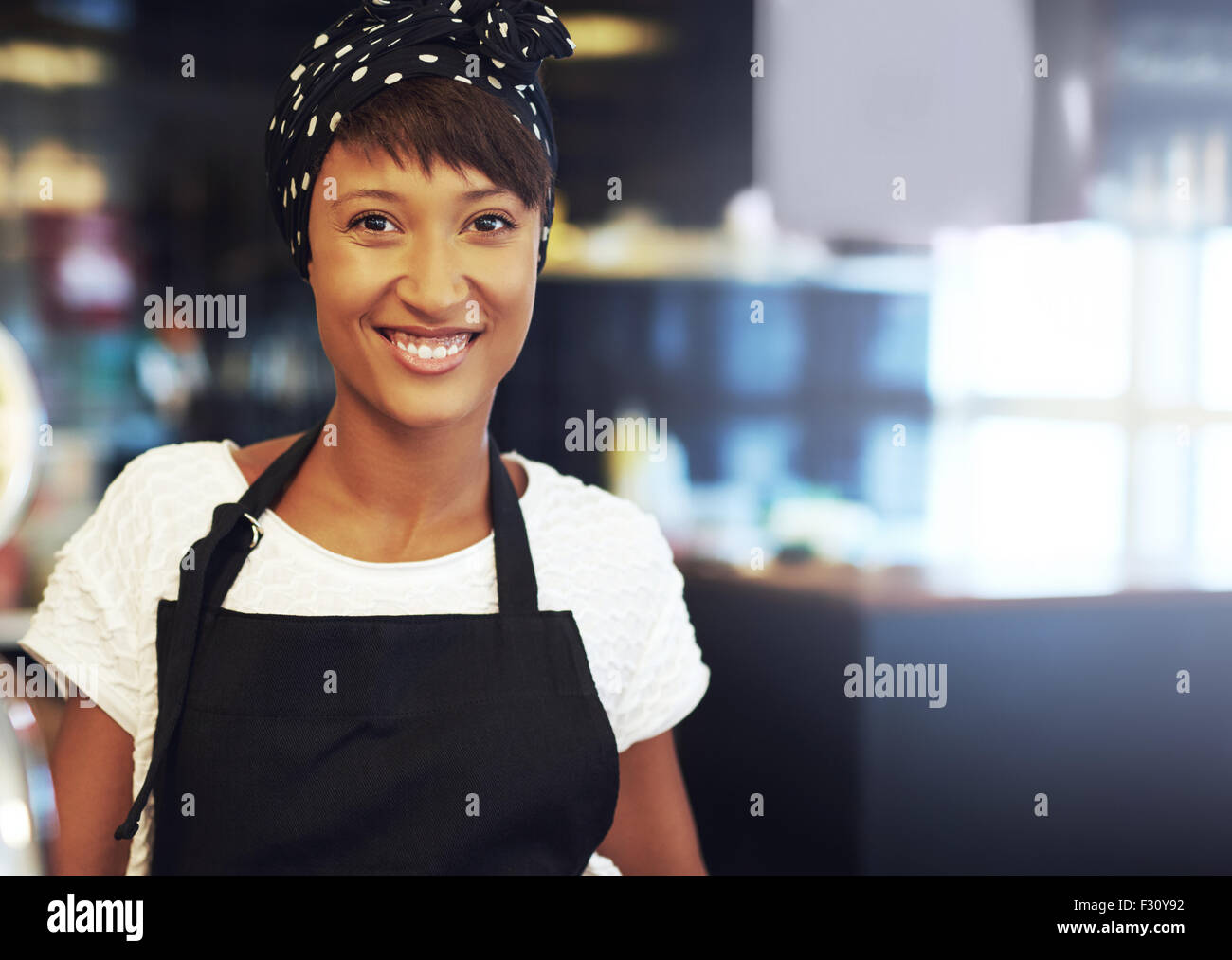 Jeunes business owner standing dans son café-restaurant dans un tablier et bandana smiling at the camera Banque D'Images