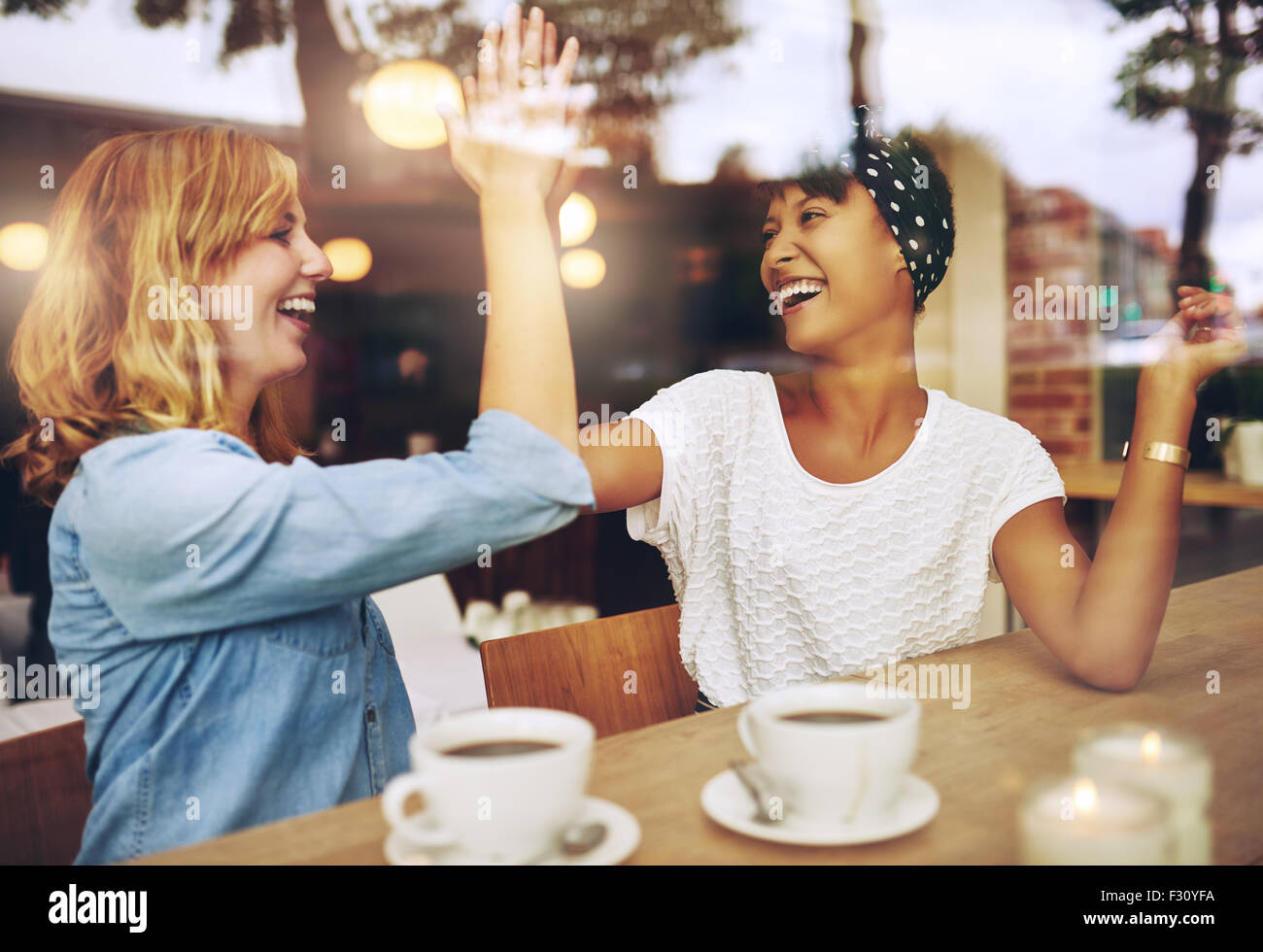 Jeune fille exubérante heureux amis donnant une forte cinq gifles chaque autres part en félicitations, assis ensemble dans un café. Banque D'Images