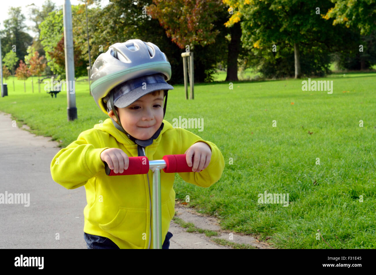 Un jeune garçon jouant avec son scooter dans le parc. Banque D'Images