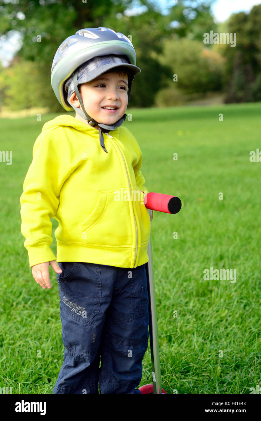 Un jeune garçon jouant avec son scooter dans le parc. Banque D'Images
