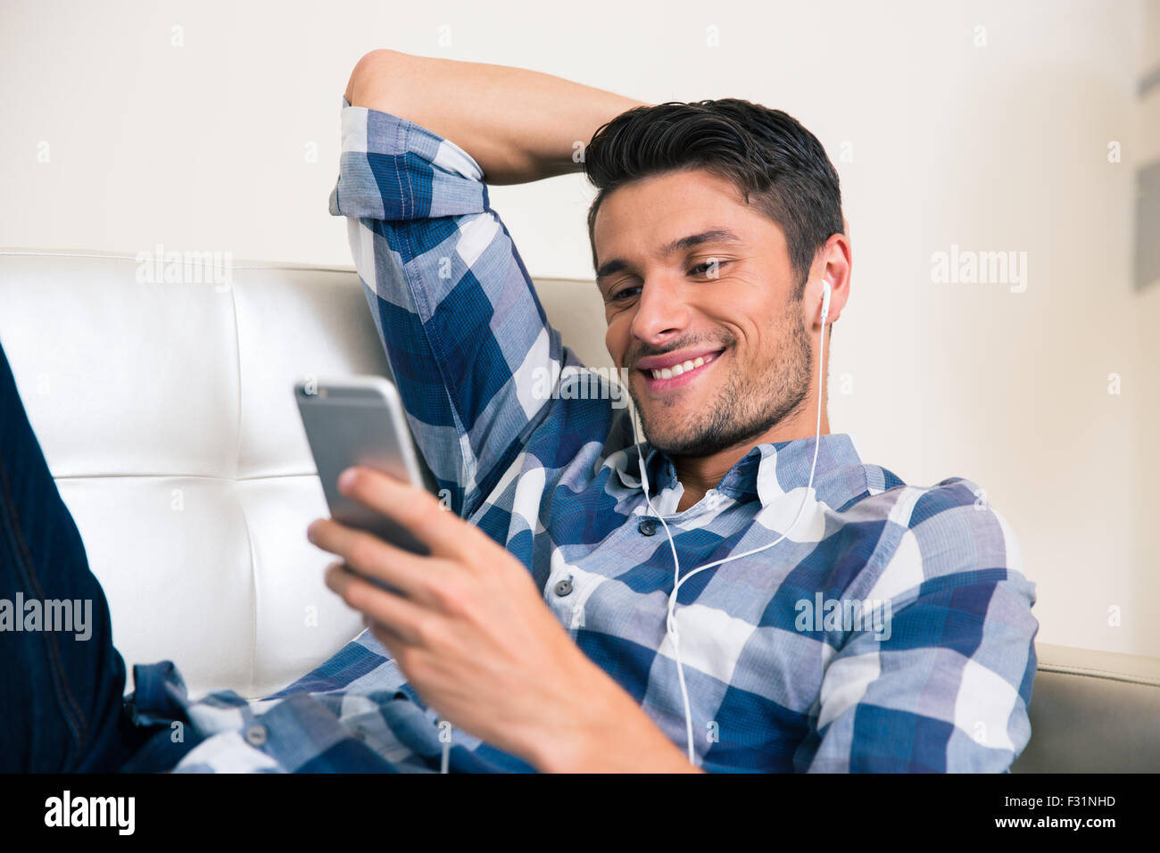 Portrait of a smiling man using smartphone sur le canapé à la maison Banque D'Images