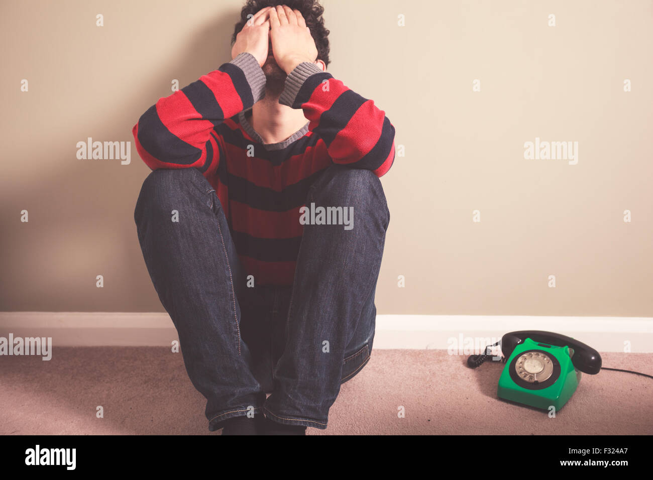 Triste et fatigué jeune homme est assis sur le plancher avec un téléphone à côté de lui Banque D'Images