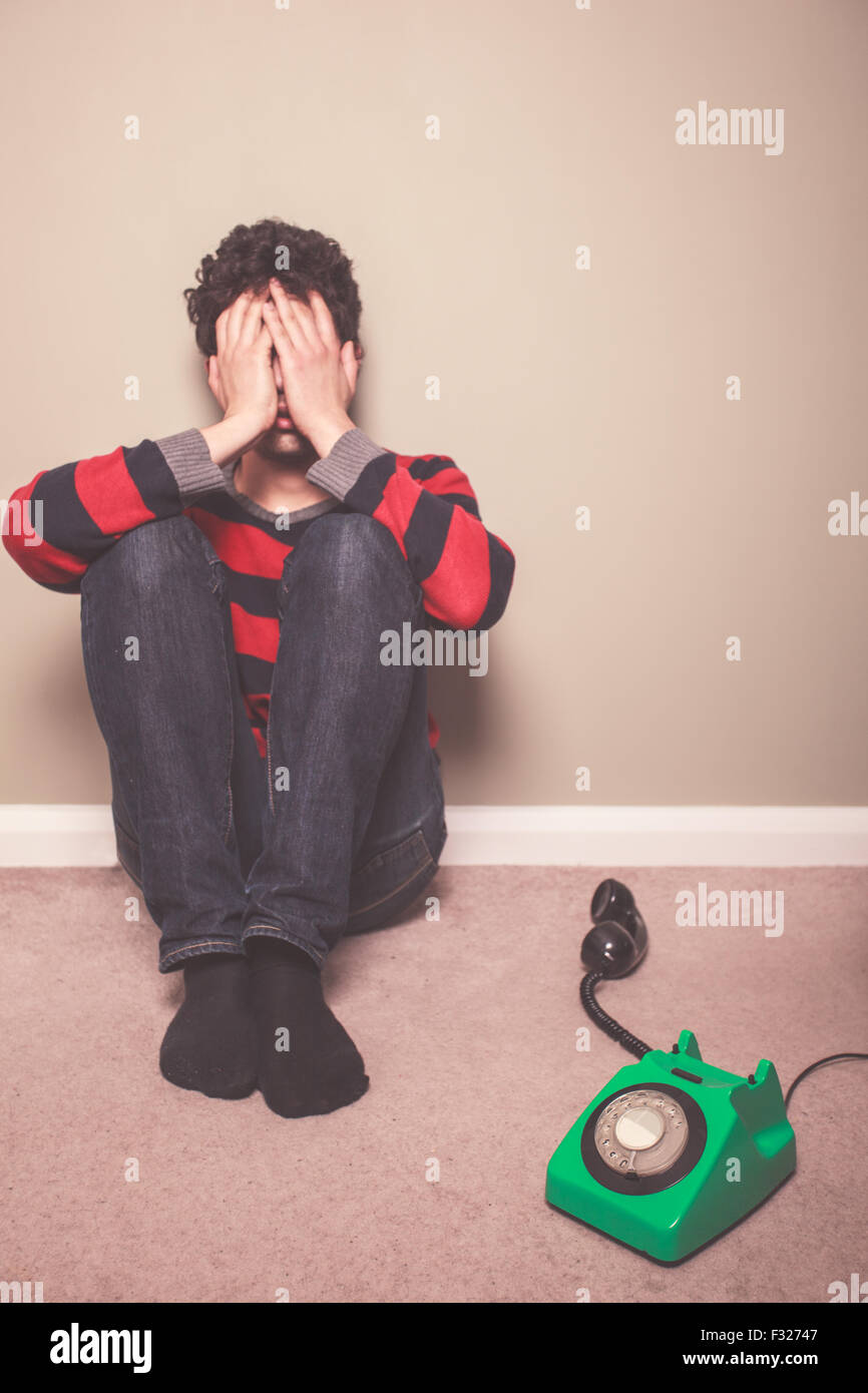 Fatigué et triste jeune homme est assis sur le plancher avec un téléphone Banque D'Images