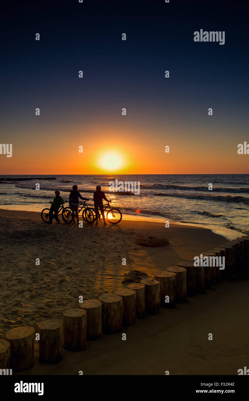 Famille avec des vélos sur la mer Baltique au coucher du soleil Banque D'Images