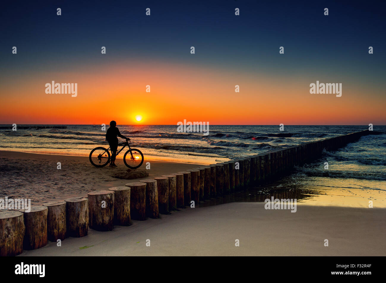 Femme avec des vélos sur la mer Baltique au coucher du soleil Banque D'Images