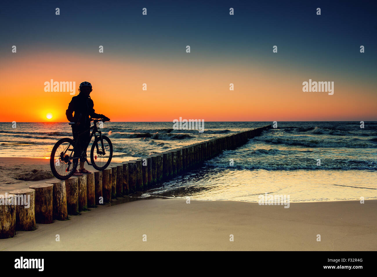 Femme avec des vélos sur la mer Baltique au coucher du soleil Banque D'Images