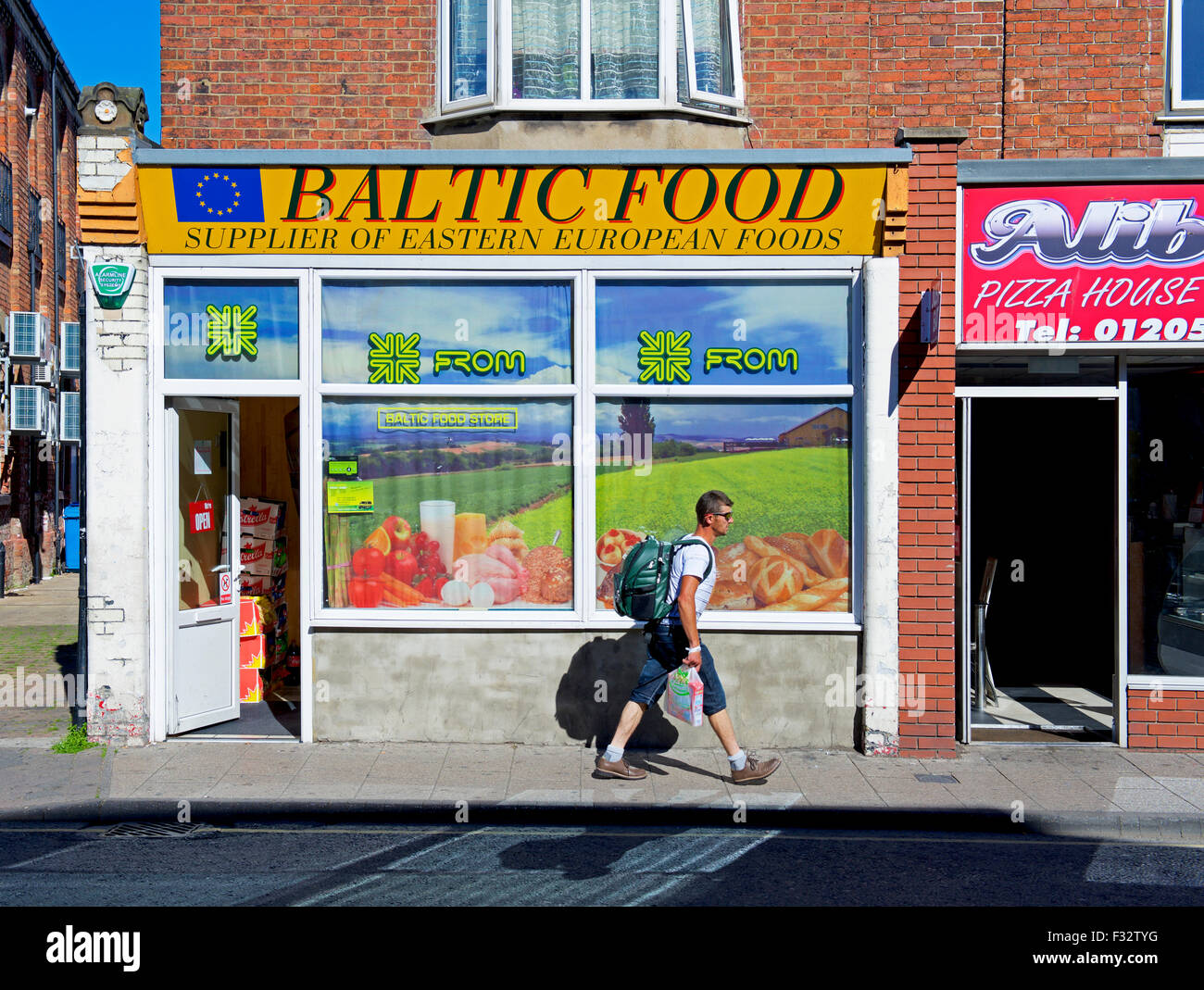 Jeune homme marchant passé boutique de produits alimentaires d'Europe de l'est à Boston, Lincolnshire, Angleterre, Royaume-Uni Banque D'Images