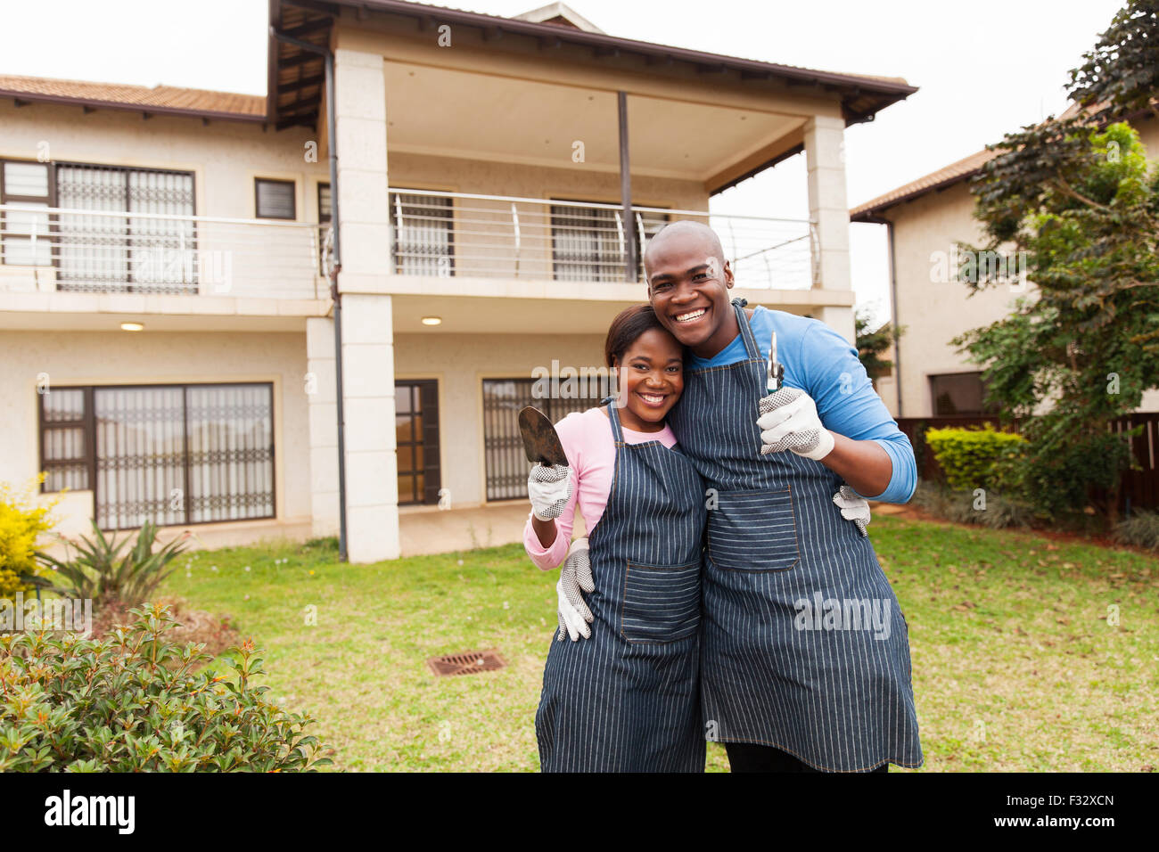 Cheerful young couple holding permanent d'outils de jardinage dans la cour avant Banque D'Images