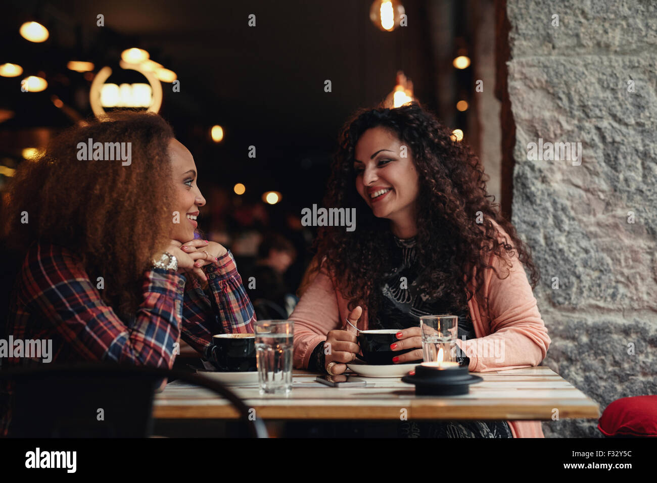 Deux femmes discutant dans un restaurant en souriant. Jeunes amis assis dans un café et parler. Banque D'Images