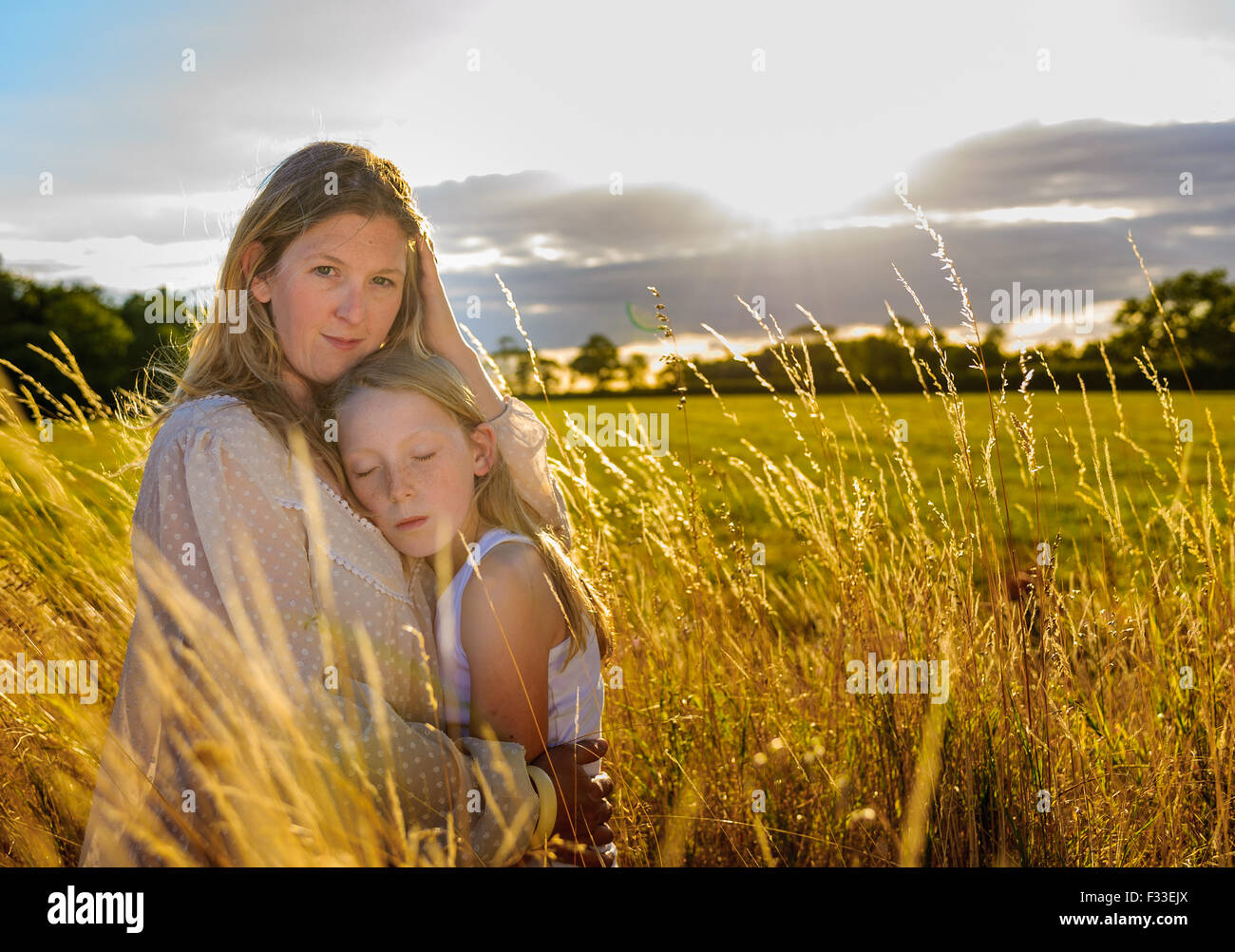 Un portrait en contre-jour d'une femme (de 25 à 30) avec sa fille (8 ans) assis dans dans un champ d'herbe haute sur un soir d'été Banque D'Images