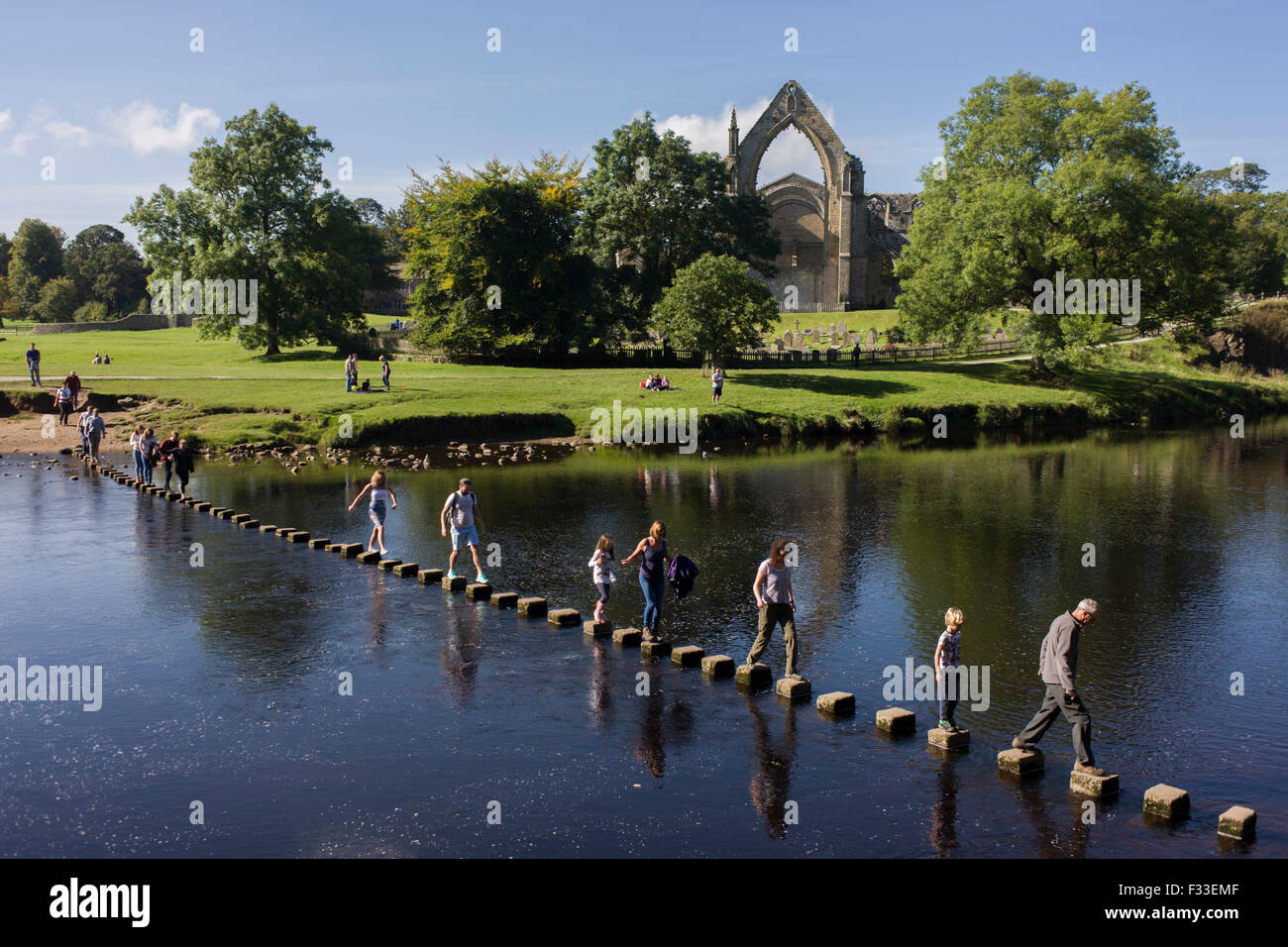 Les familles risquent de se retrouver dans la rivière Wharfedale en marchant sur les pierres de gué au prieuré augustinien Bolton, Yorkshire du Nord. Banque D'Images
