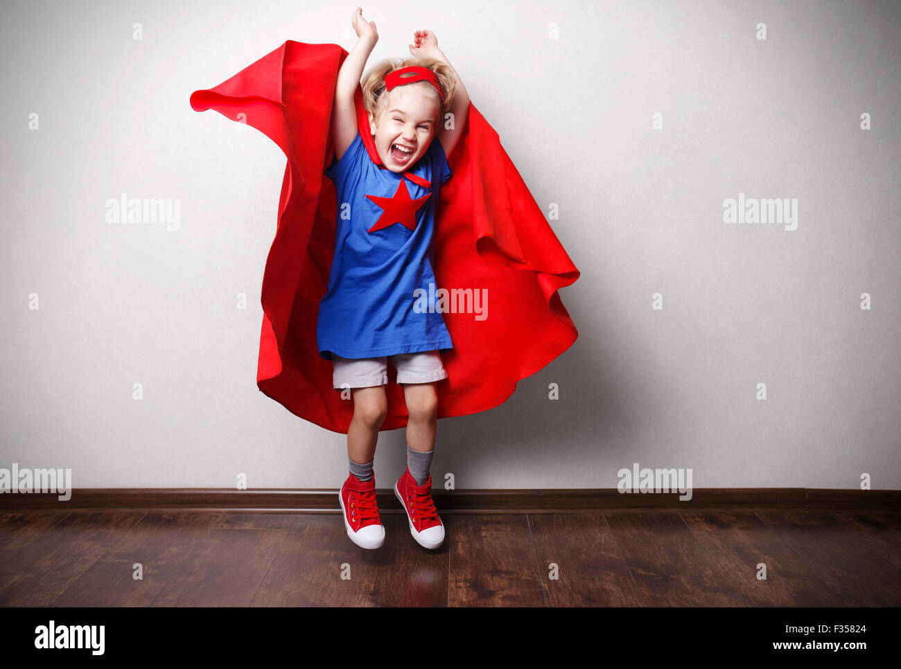 Heureux l'enfant en costume de super-héros contre mur gris. Banque D'Images