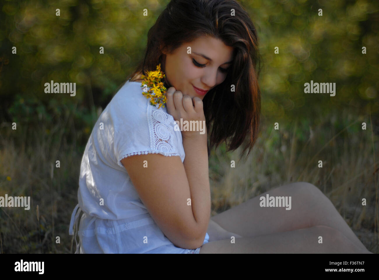 Belle fille à la recherche vers le bas avec des fleurs jaunes dans ses mains dans une robe blanche Banque D'Images