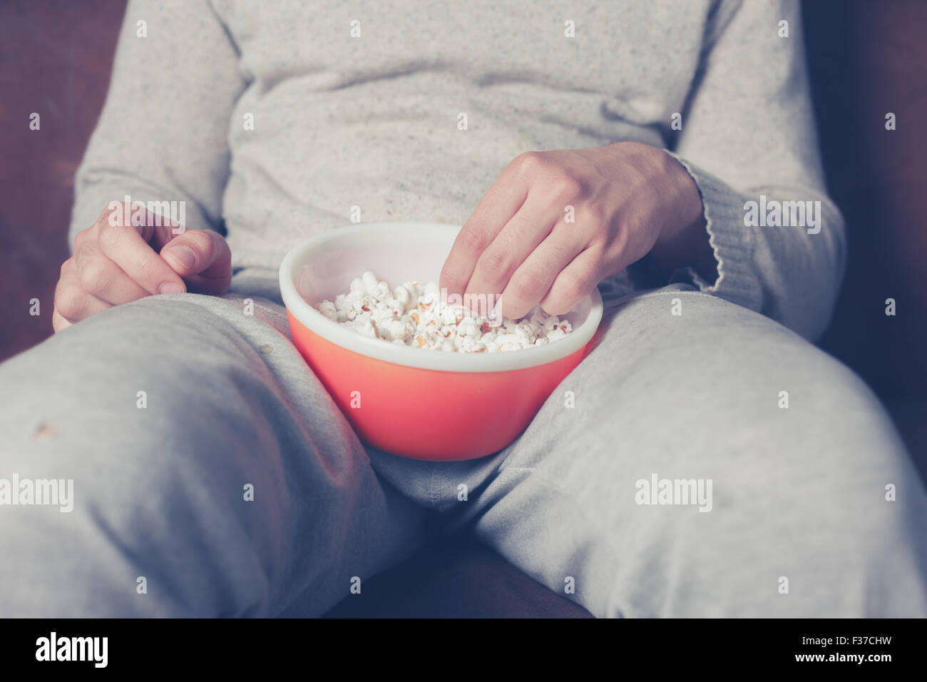 Jeune homme assis sur un canapé et eating popcorn Banque D'Images