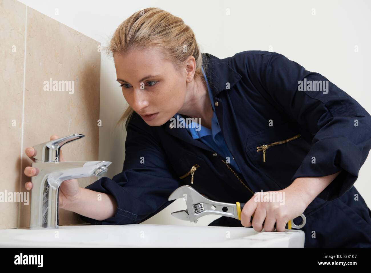 Femme plombier travaillant sur l'évier à l'aide d'une clé Banque D'Images