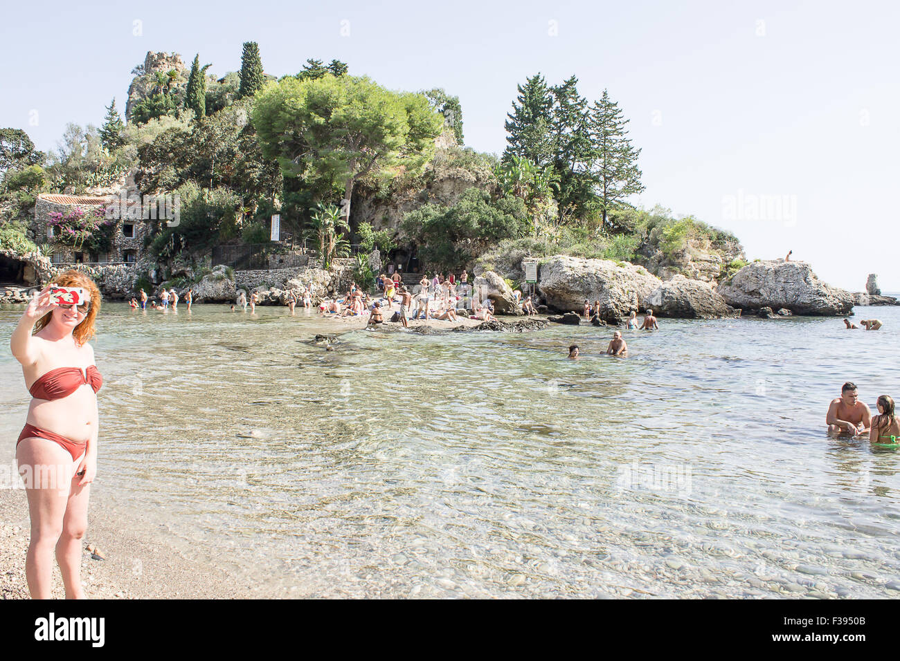 Une jeune dame cheveux gingembre en tenant un selfi avec son téléphone mobile de l'île Isola Bella en Sicile. Banque D'Images