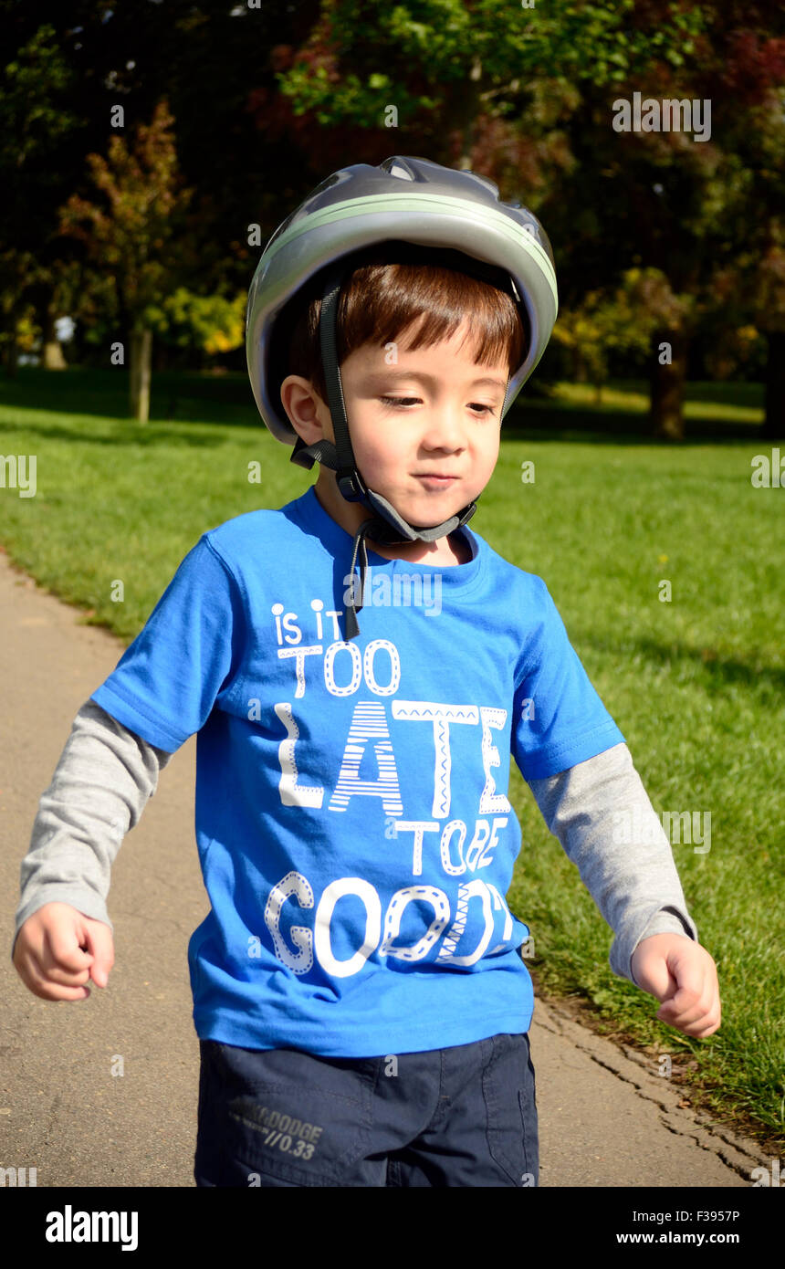 Un jeune garçon portant un casque de vélo dans le parc. Banque D'Images