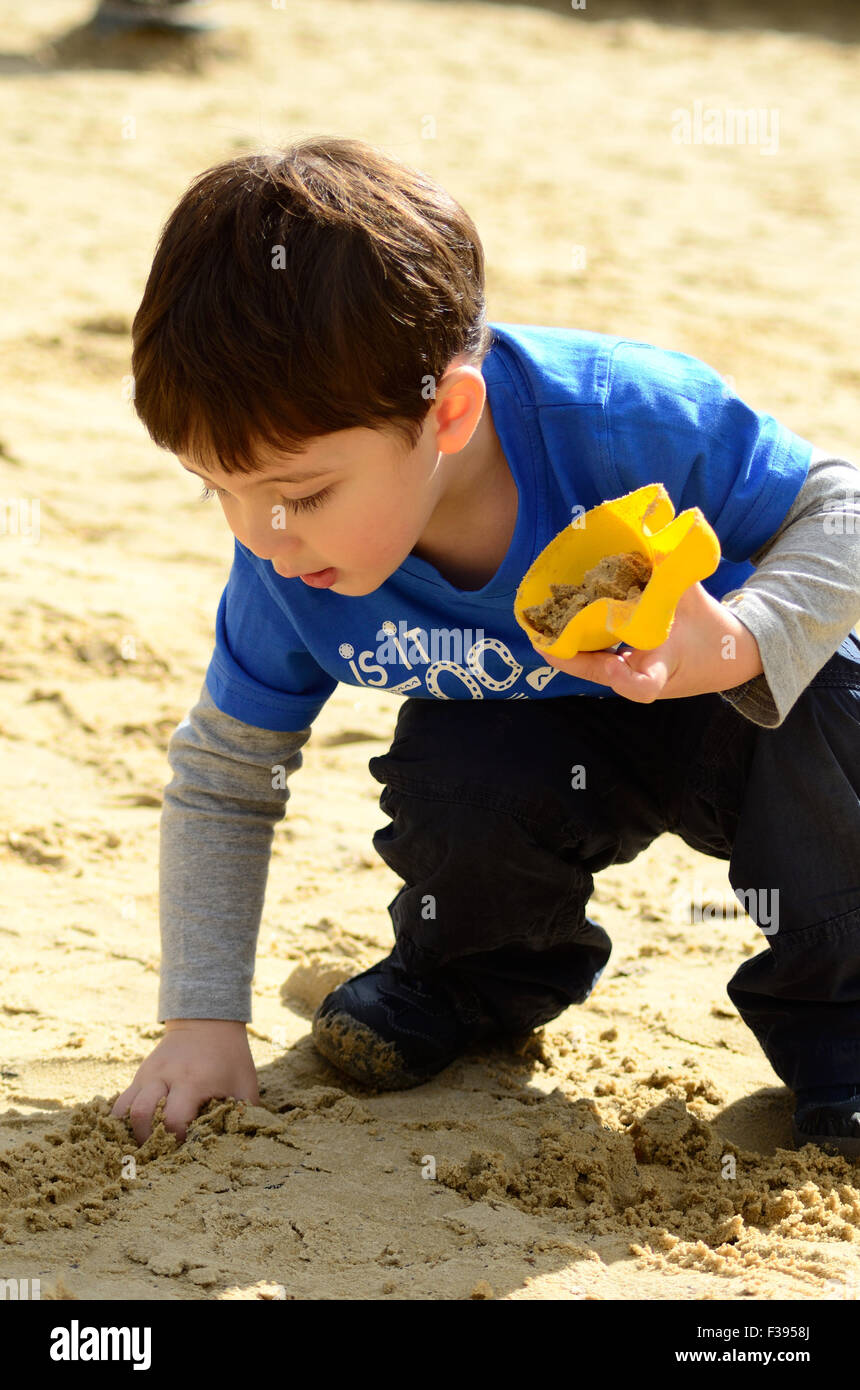 Un jeune garçon joue avec le sable dans l'aire de jeux dans le parc. Banque D'Images