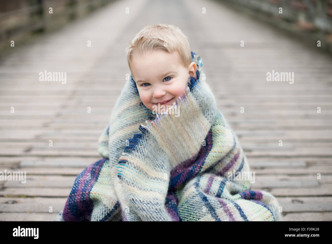 Portrait d'un garçon enveloppé dans une couverture, assis sur un pont en bois Banque D'Images