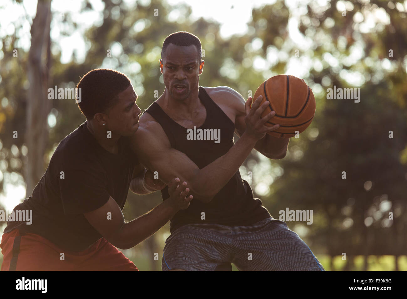 Deux jeunes hommes jouant au basket-ball dans le parc au coucher du soleil Banque D'Images