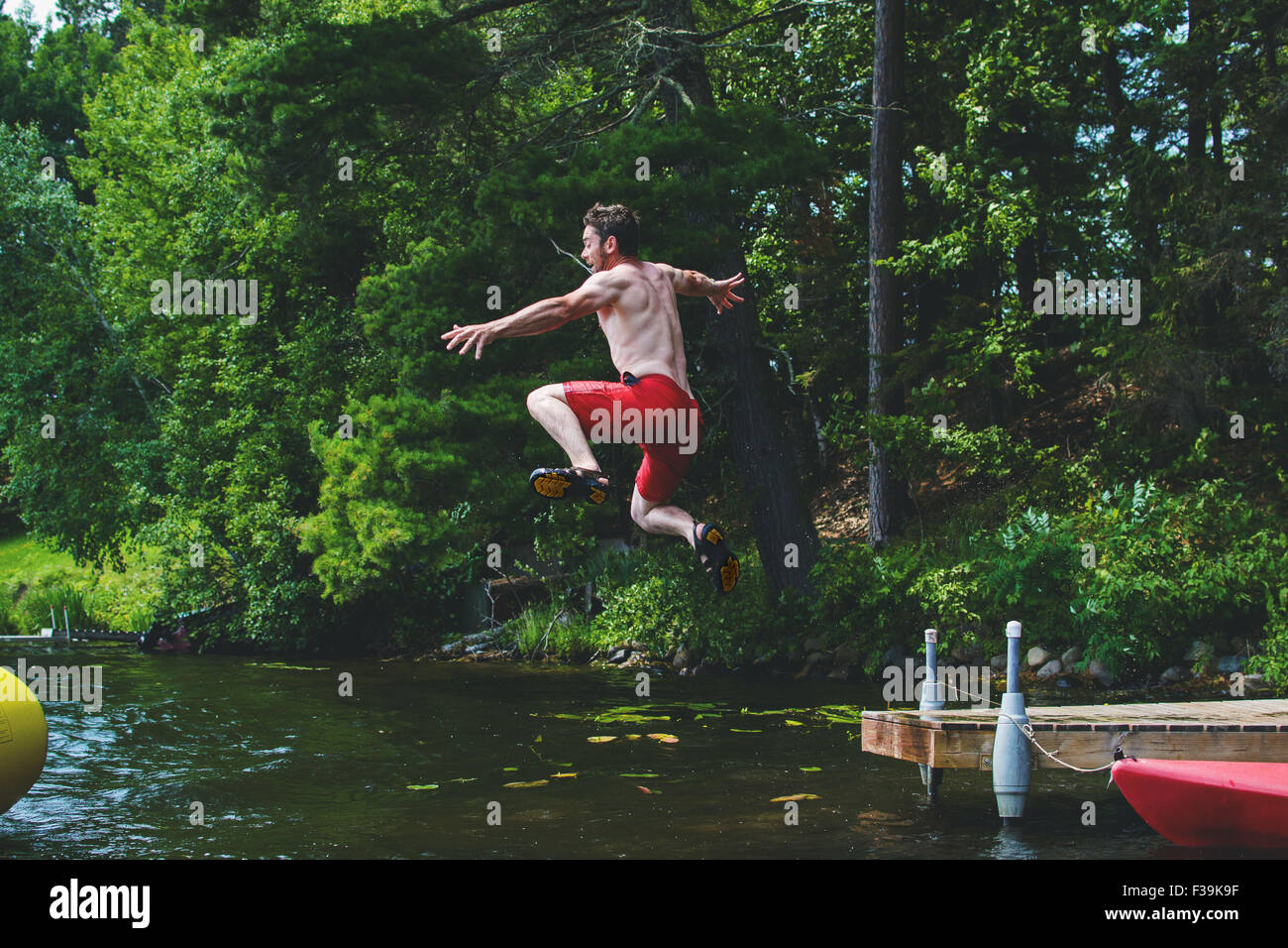 Homme sautant hors d'une jetée dans un lac Banque D'Images