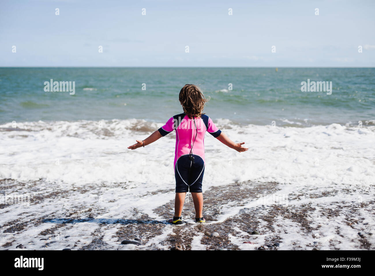Vue Arriere D Une Jeune Fille Dans Un Wetsuit Standing Dans Le Surf Sur La Plage Avec Ses Bras Tendus Photo Stock Alamy