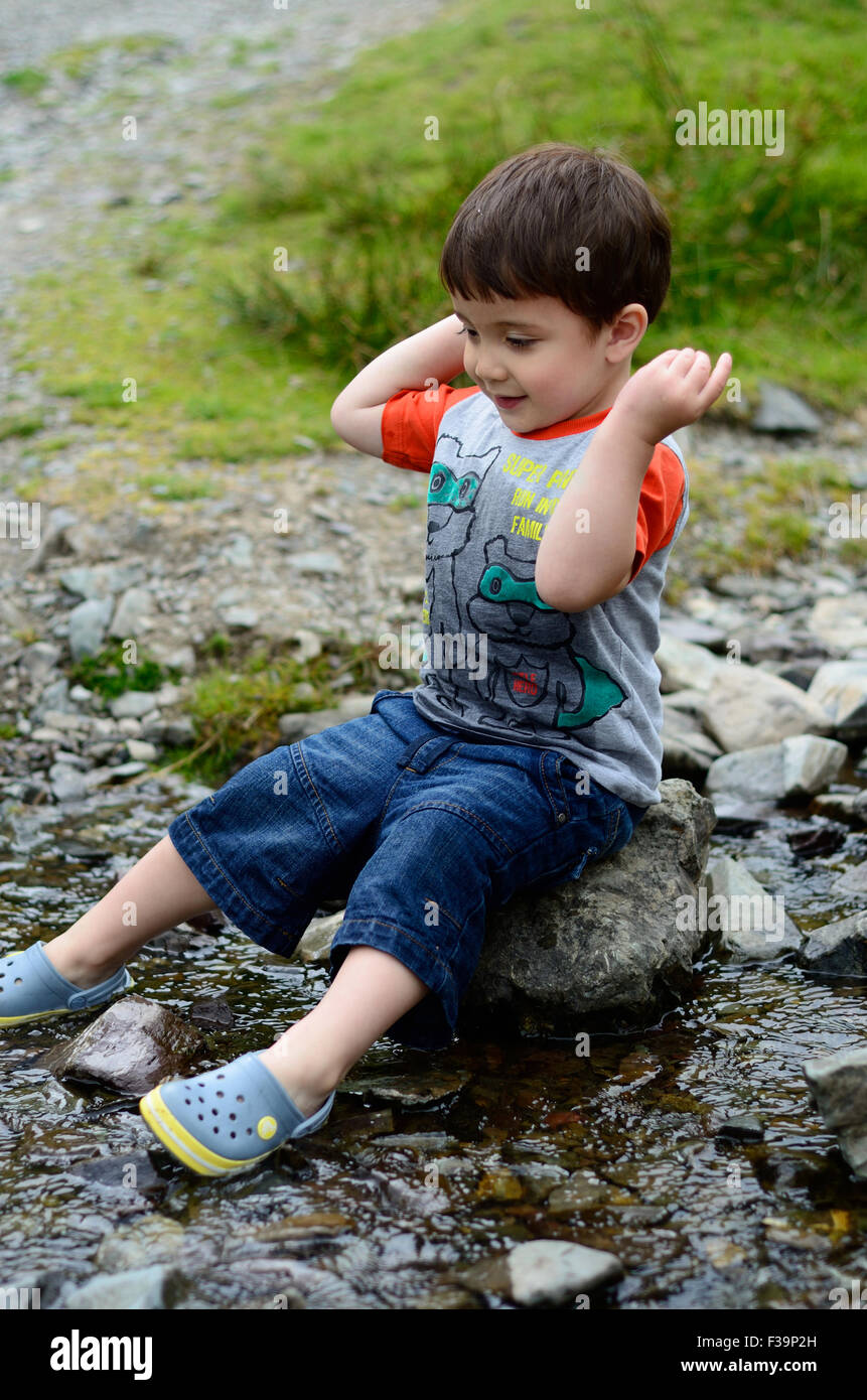 Un jeune garçon est assis sur un rocher au milieu d'un ruisseau Banque D'Images