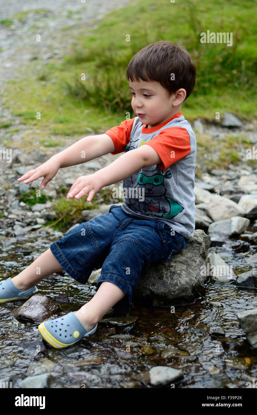 Un jeune garçon est assis sur un rocher au milieu d'un ruisseau Banque D'Images