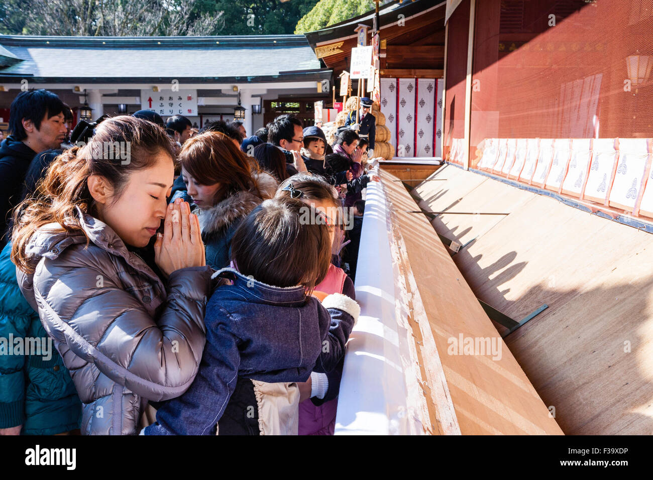 Le Japon, la nouvelle année, l'hiver. Femme japonaise, mère, tenant la main et priant avec deux enfants mineurs au sanctuaire Shinto bondé. La journée. Banque D'Images