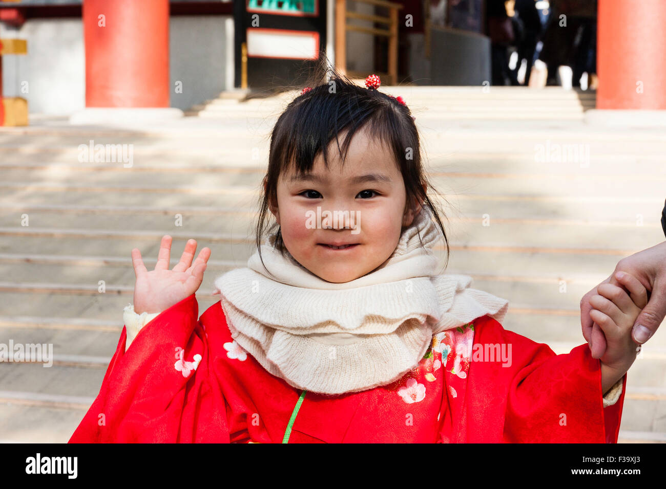L'enfant japonais, girl, de 3-4 ans, en kimono rouge, signe d'événements et de sourire. Close up, tête et épaule tourné, à l'extérieur en face de temple shintoïste. Banque D'Images