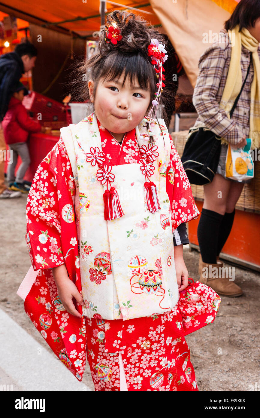 Petite Japonaise vieille de cinq ans, un peu plus de poids avec joues potelées, debout posant pour viewer en portant un kimono rose et rouge. Chauds d'expression. Banque D'Images