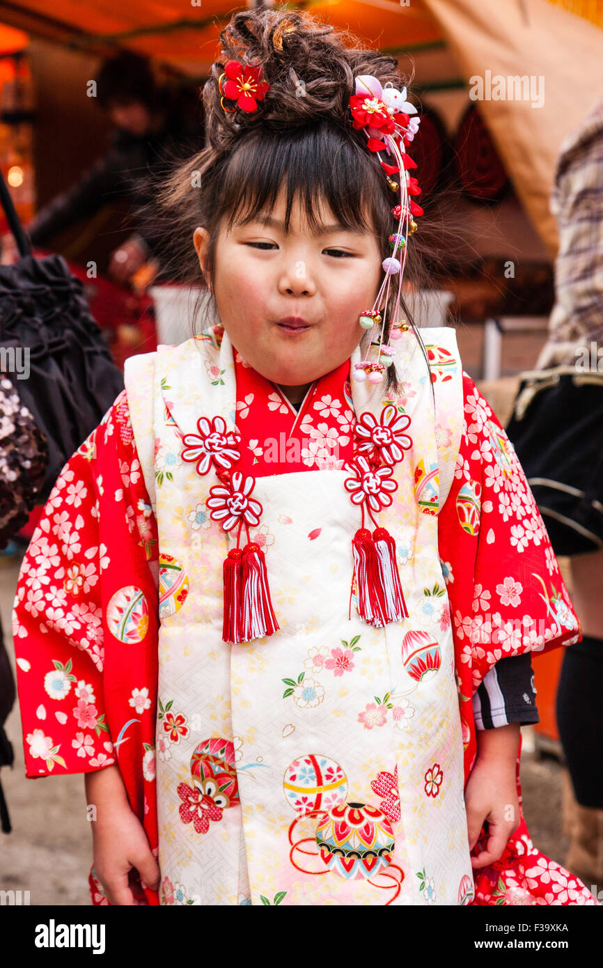 Petite Japonaise vieille de cinq ans, un peu plus de poids avec joues potelées, debout posant pour viewer en portant un kimono rose et rouge. Chauds d'expression. Banque D'Images