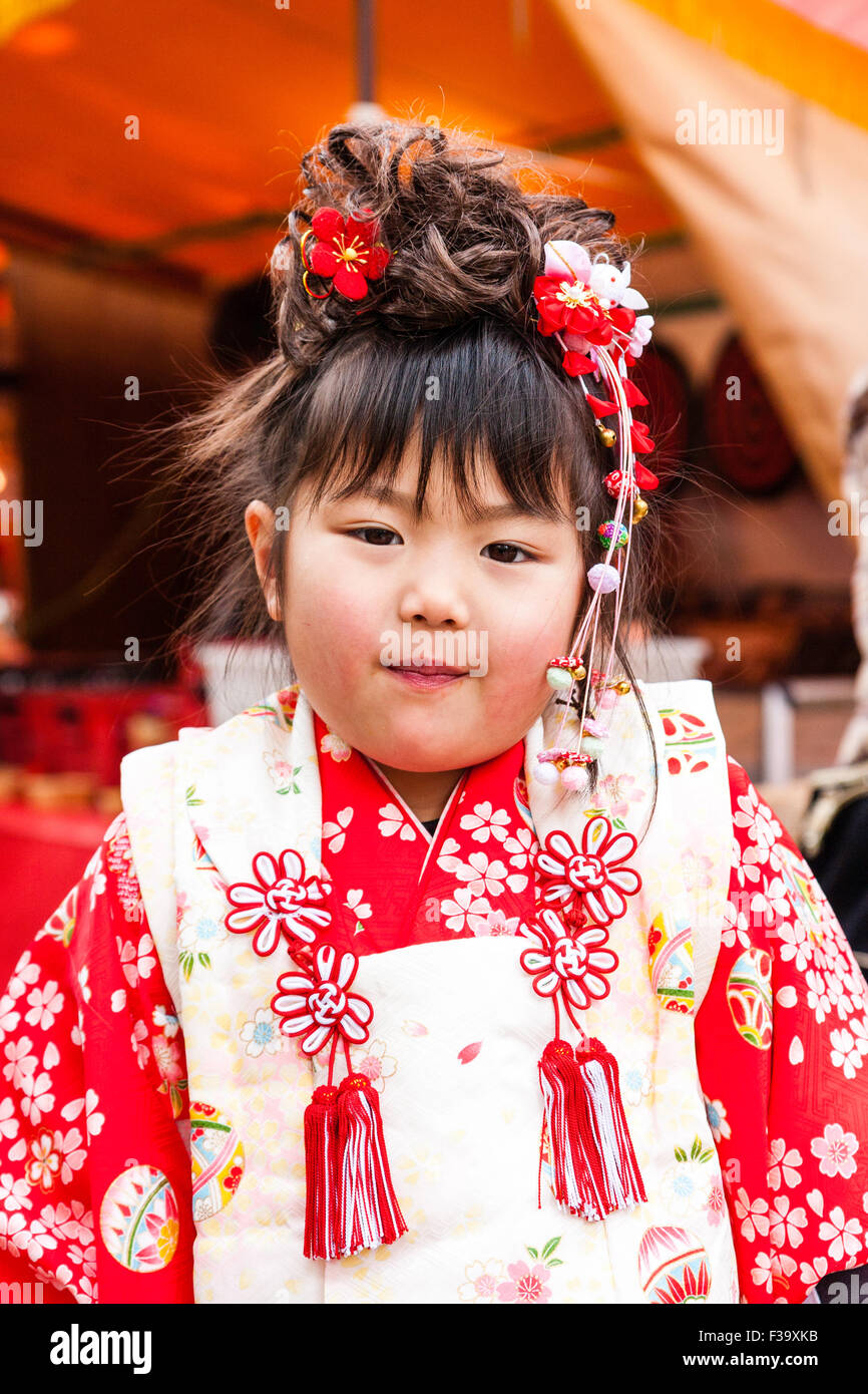 Petite Japonaise vieille de cinq ans, un peu plus de poids avec joues potelées, debout posant pour viewer en portant un kimono rose et rouge. Chauds d'expression. Banque D'Images