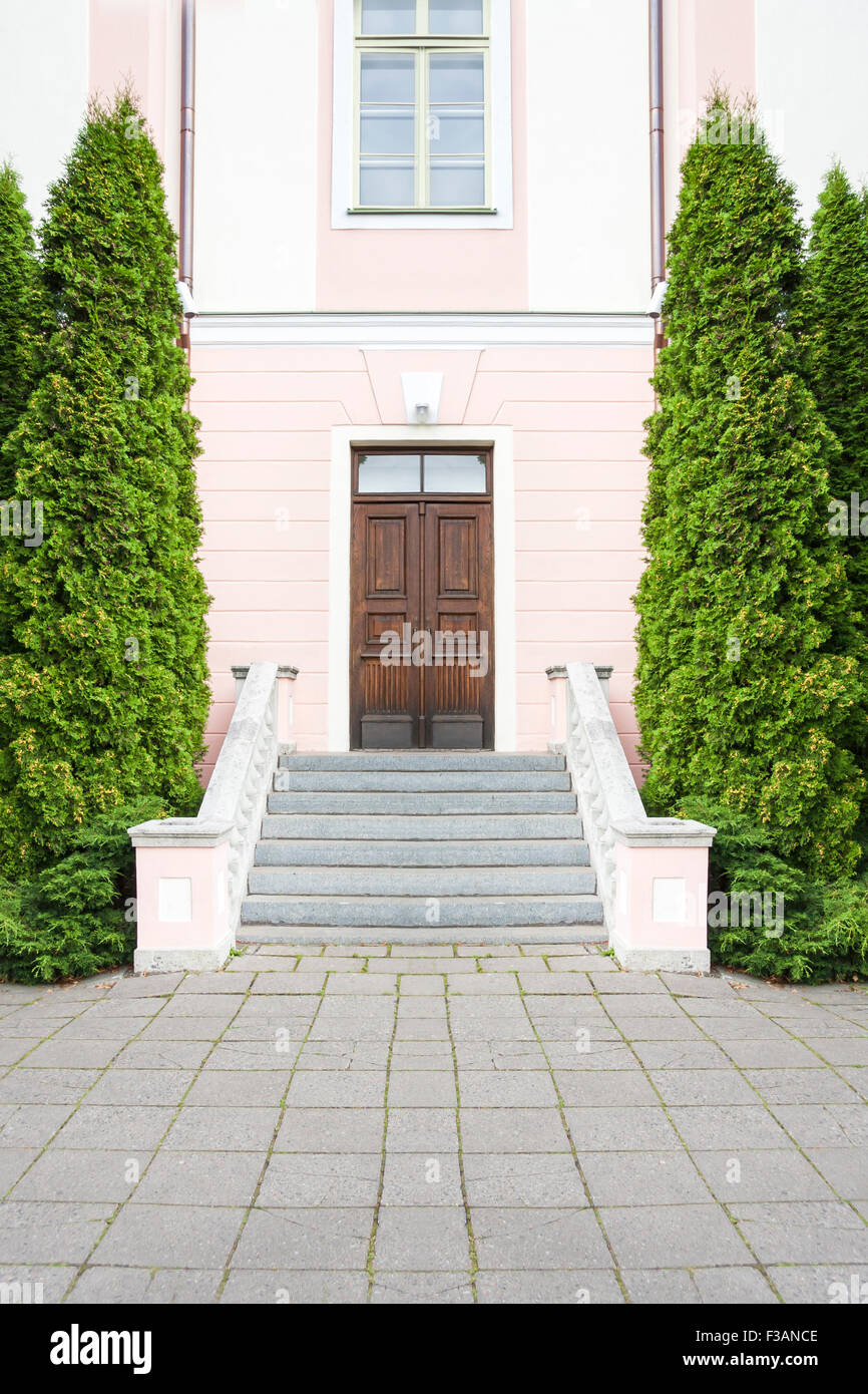 Escalier avec de grands arbres verts d'apartés menant à une maison en pierre rose avec une porte en bois brun foncé Banque D'Images
