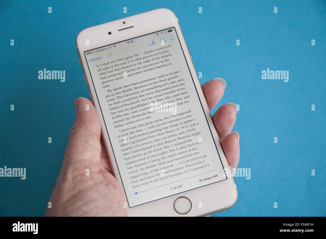 La lecture d'un ebook sur un or et blanc Apple iPhone 6 againdt un fond bleu Banque D'Images