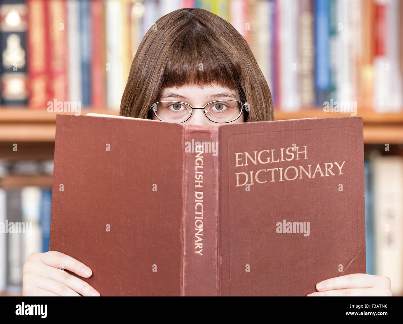 Fille avec des lunettes donne sur English Dictionary livre et bibliothèque sur l'arrière-plan Banque D'Images