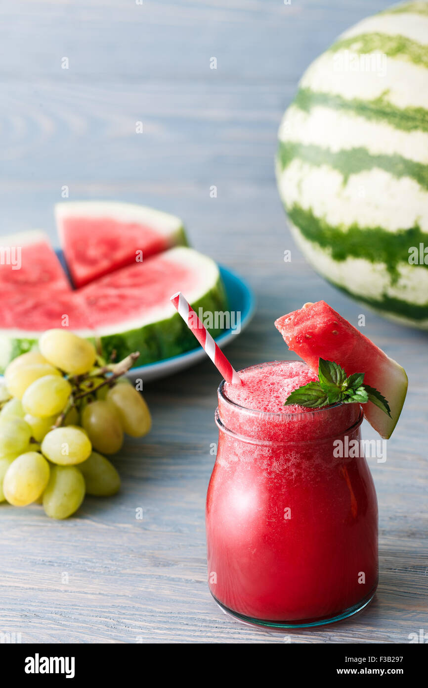 Smoothie melon d'eau lumineuse garnie d'un morceau de melon et de feuilles de menthe bleu sur fond de bois. Banque D'Images