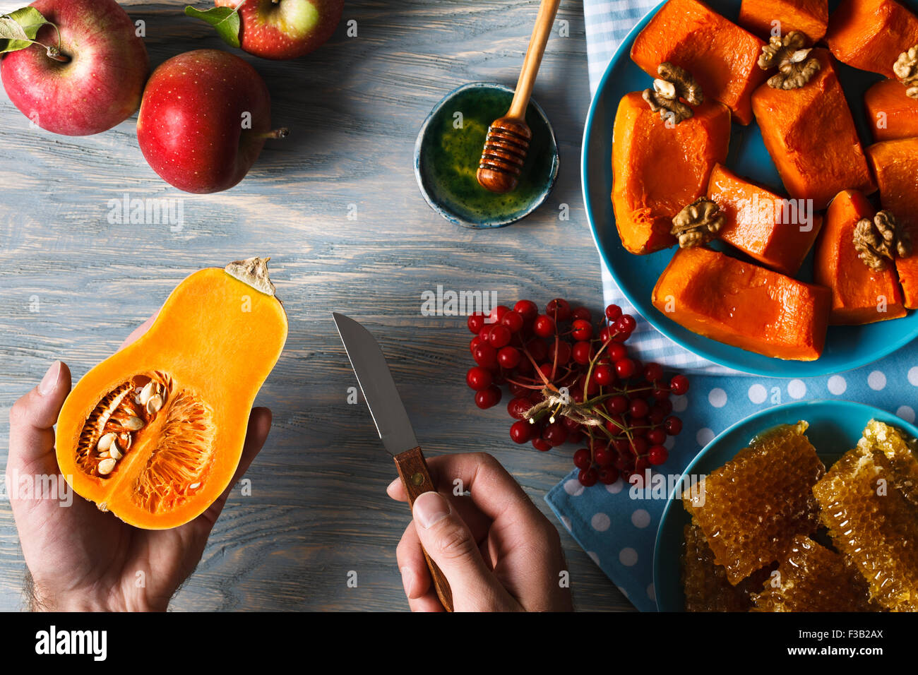 Menu d'automne. Homme mains tenant peu citrouille et un couteau dans le contexte des pommes fraîches, un tas de petits fruits viburnum, h Banque D'Images