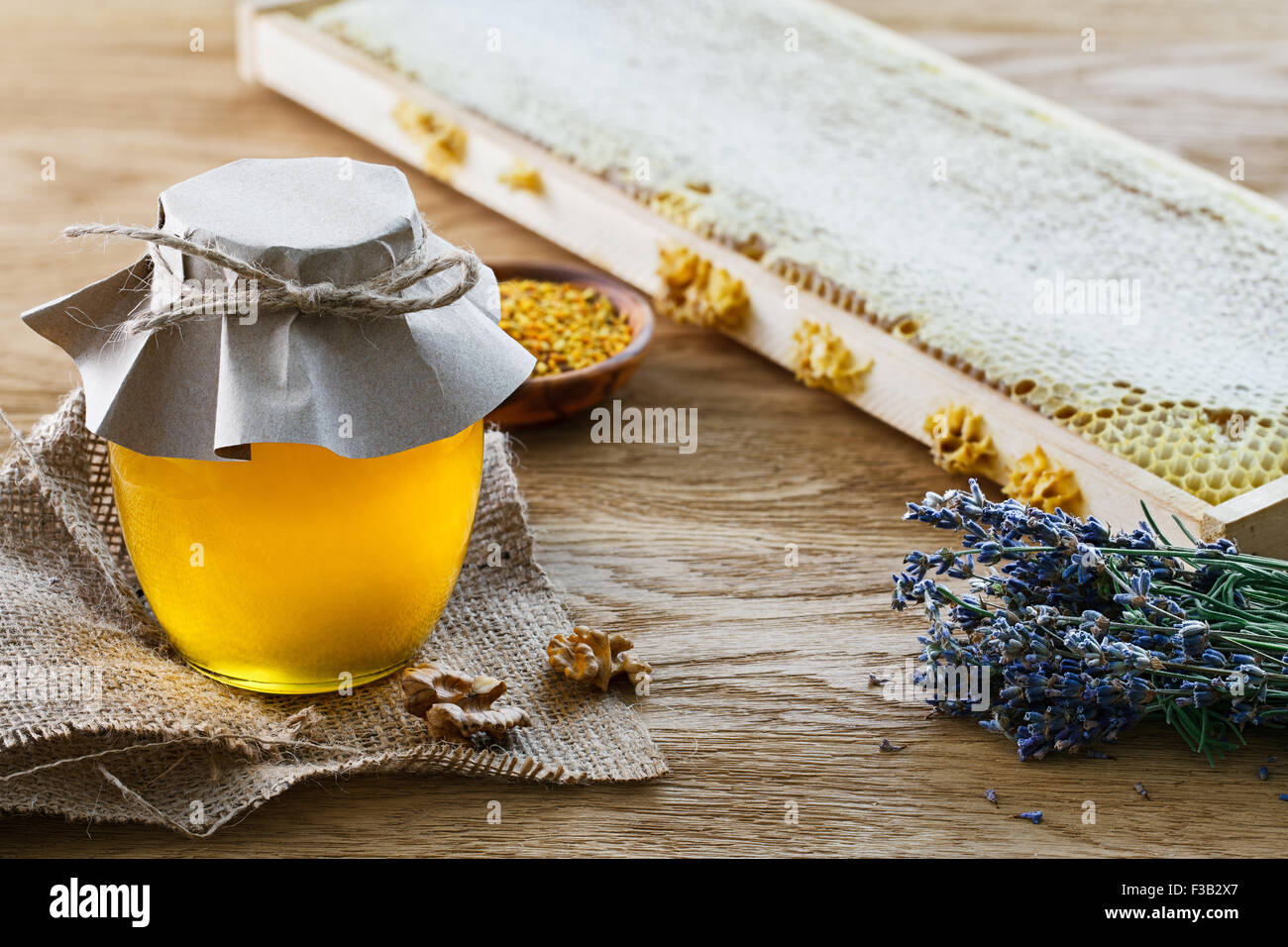 Pot en verre rempli de miel, un bouquet de lavande, d'abeilles et d'un bol en t avec du pollen d'abeille sur fond de bois. Banque D'Images