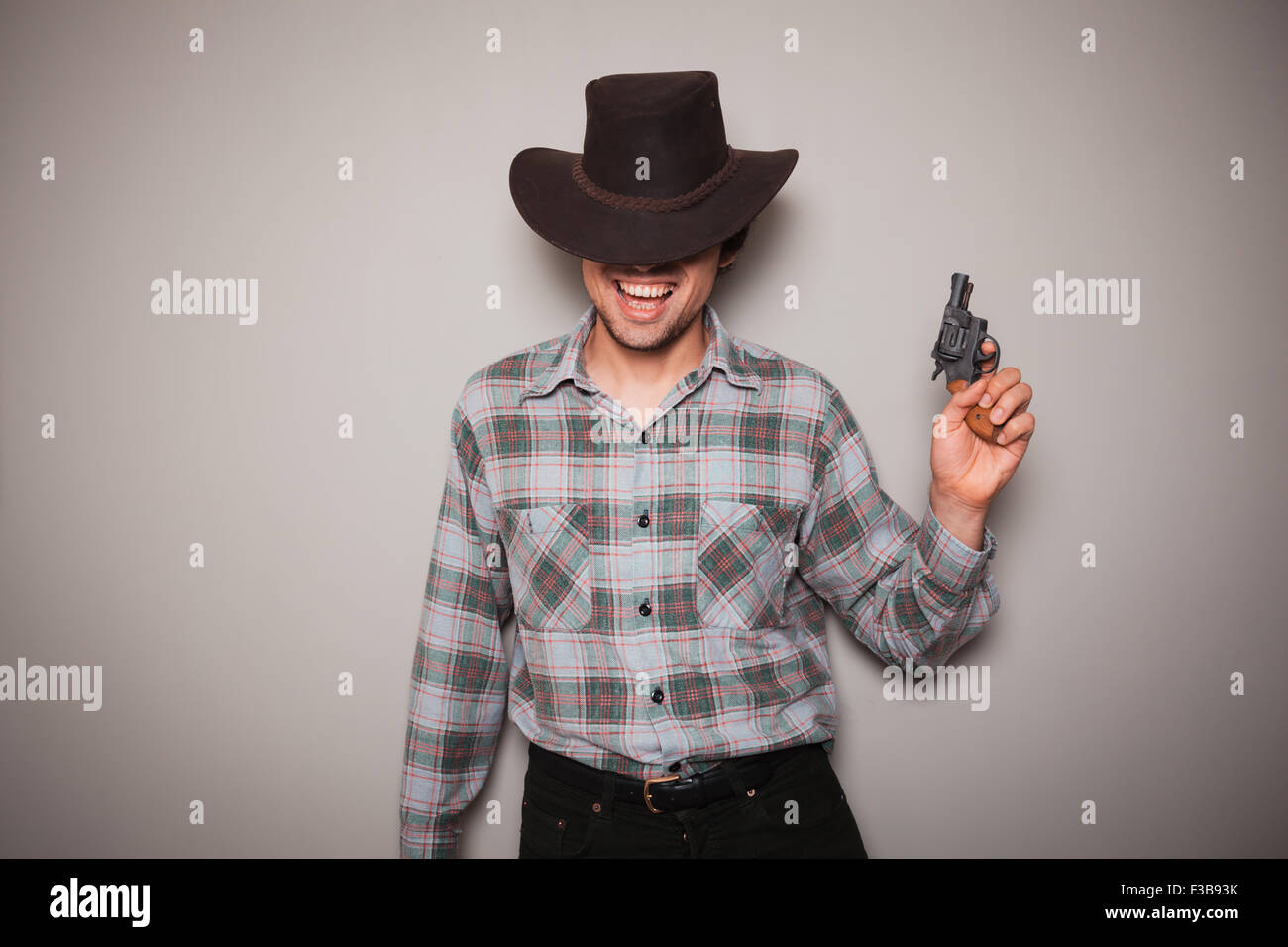 Un jeune homme portant un chapeau de cowboy et un plaid shirt tient un revolver Banque D'Images