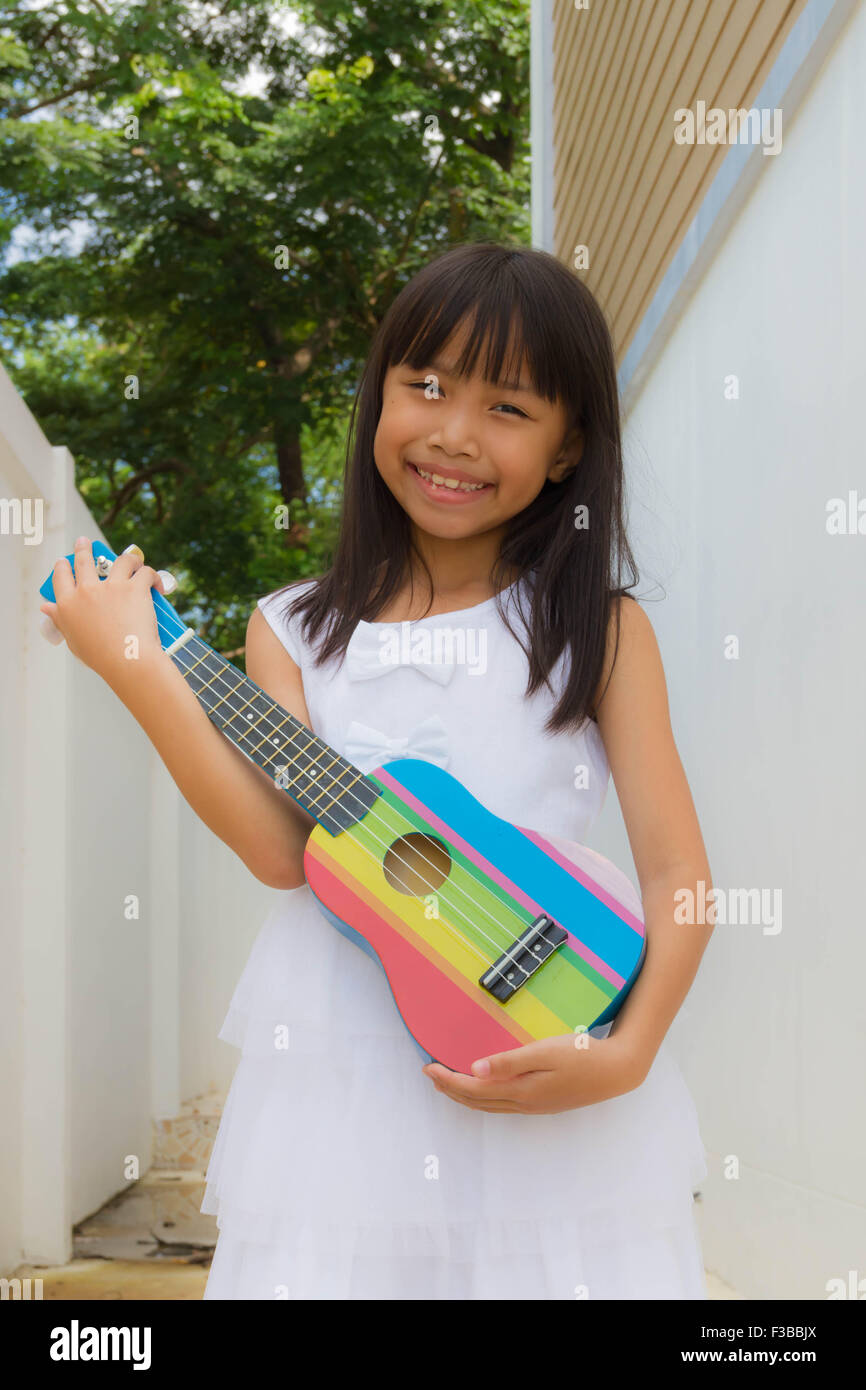 Young Asian Funny Girl s'amusant et en jouant sur les petits guitare ukulele colorés Banque D'Images