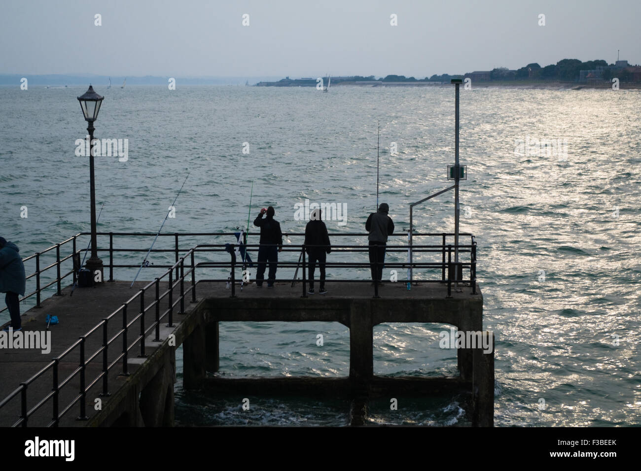 3 personnes pêchent à partir d'un quai dans le port de Portsmouth, Hampshire, Angleterre. Banque D'Images