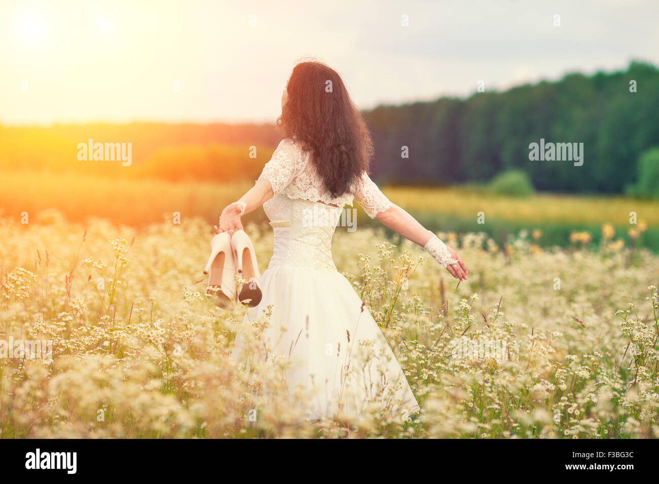 Young bride holding shoes walking on the flower meadow Banque D'Images