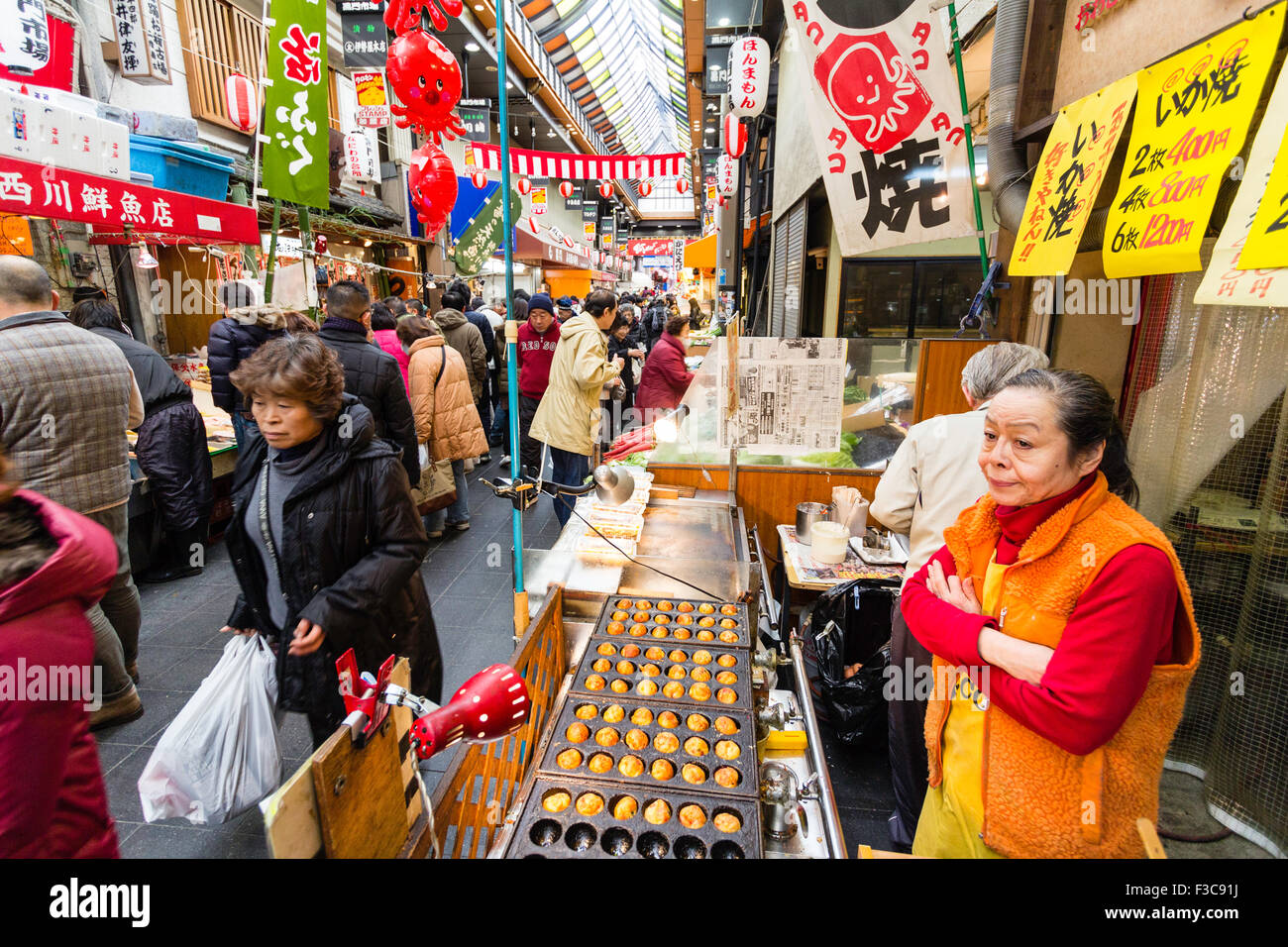 Femme debout à la friture et de la vente des boulettes de poulpe, takoyaki, dans le marché de Kuromon Ichiba à Osaka. Voir l'arcade avec en arrière-plan. Banque D'Images