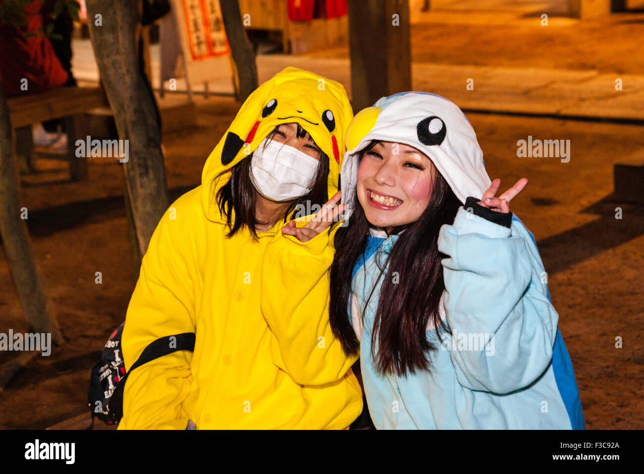 Deux jeunes femmes japonaises, l'un avec un masque, rire de spectateur et faire la paix tout en geste habillé comme Pikachu, nuit, nouvel an. Banque D'Images