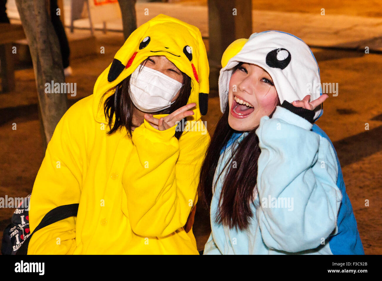 Deux jeunes femmes japonaises, l'un avec un masque, rire de spectateur et faire la paix tout en geste habillé comme Pikachu, nuit, nouvel an. Banque D'Images